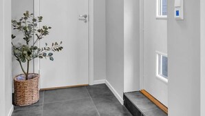 A hallway with a white door, grey tiled floor, a wicker basket with a plant, and a light fixture on the ceiling.
