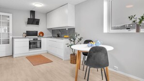 A modern kitchen with white cabinetry, a built-in oven, and a microwave. There is a dining table with chairs and a vase of flowers.