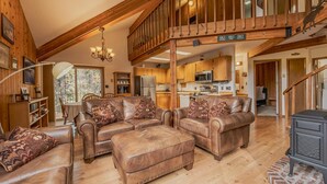A spacious living area with leather sofas, a wooden staircase, and a kitchen in the background. - Sans Souci 1, 3 Bedroom Ski In, Ski Out Retreat (Whitefish)
