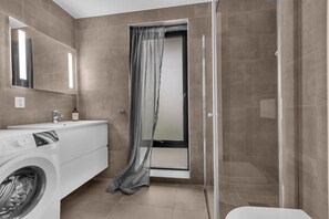 A modern bathroom with a washing machine, a sink, and a shower area. - Northstay - King`s Park (Tromsø)