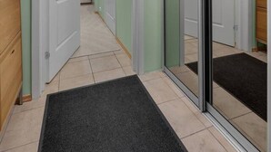A hallway with a mirrored wall, a wooden cabinet, and a black doormat.