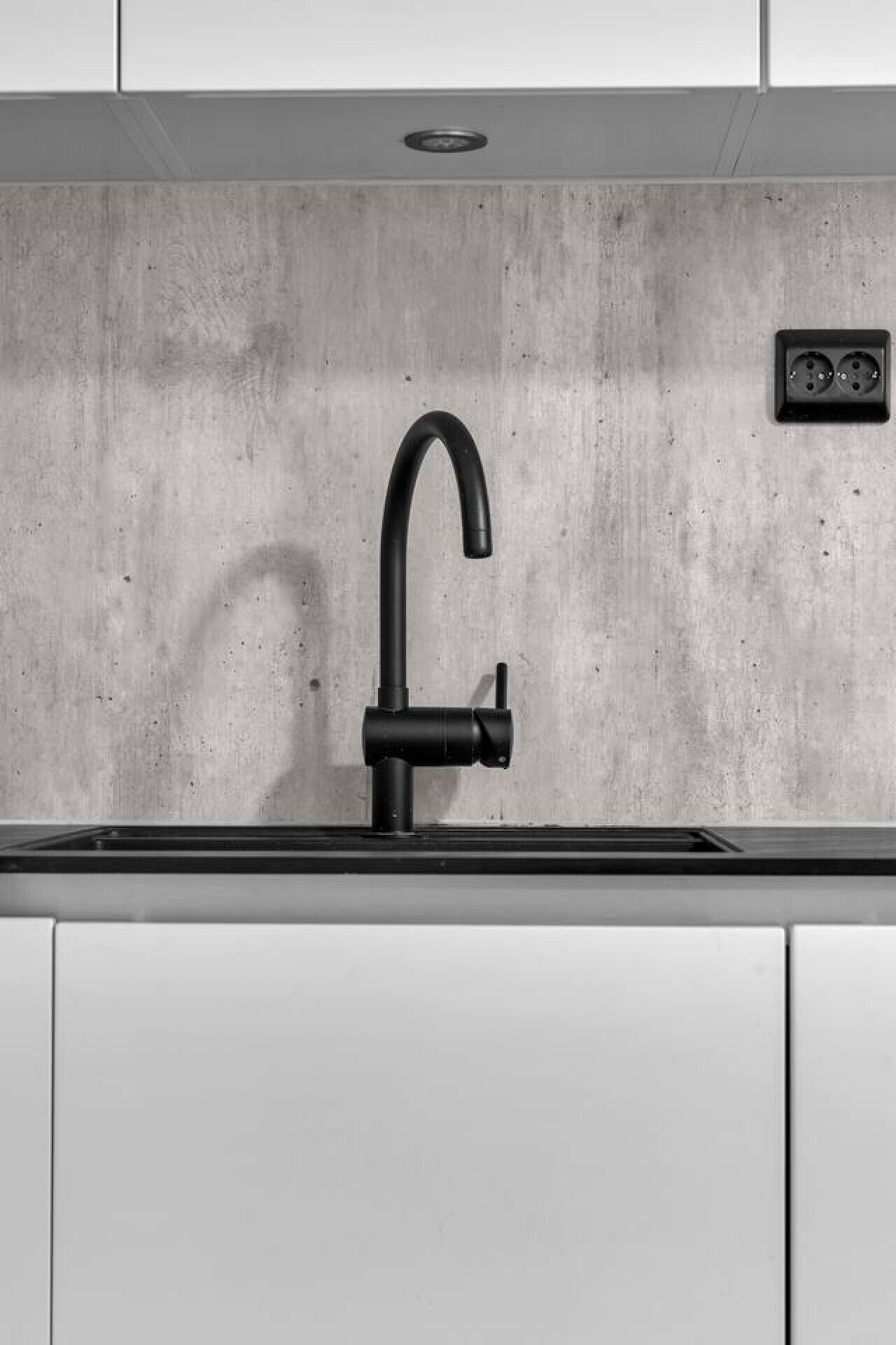 A modern kitchen with a single black faucet, a concrete backsplash, and a double electrical outlet above the sink.