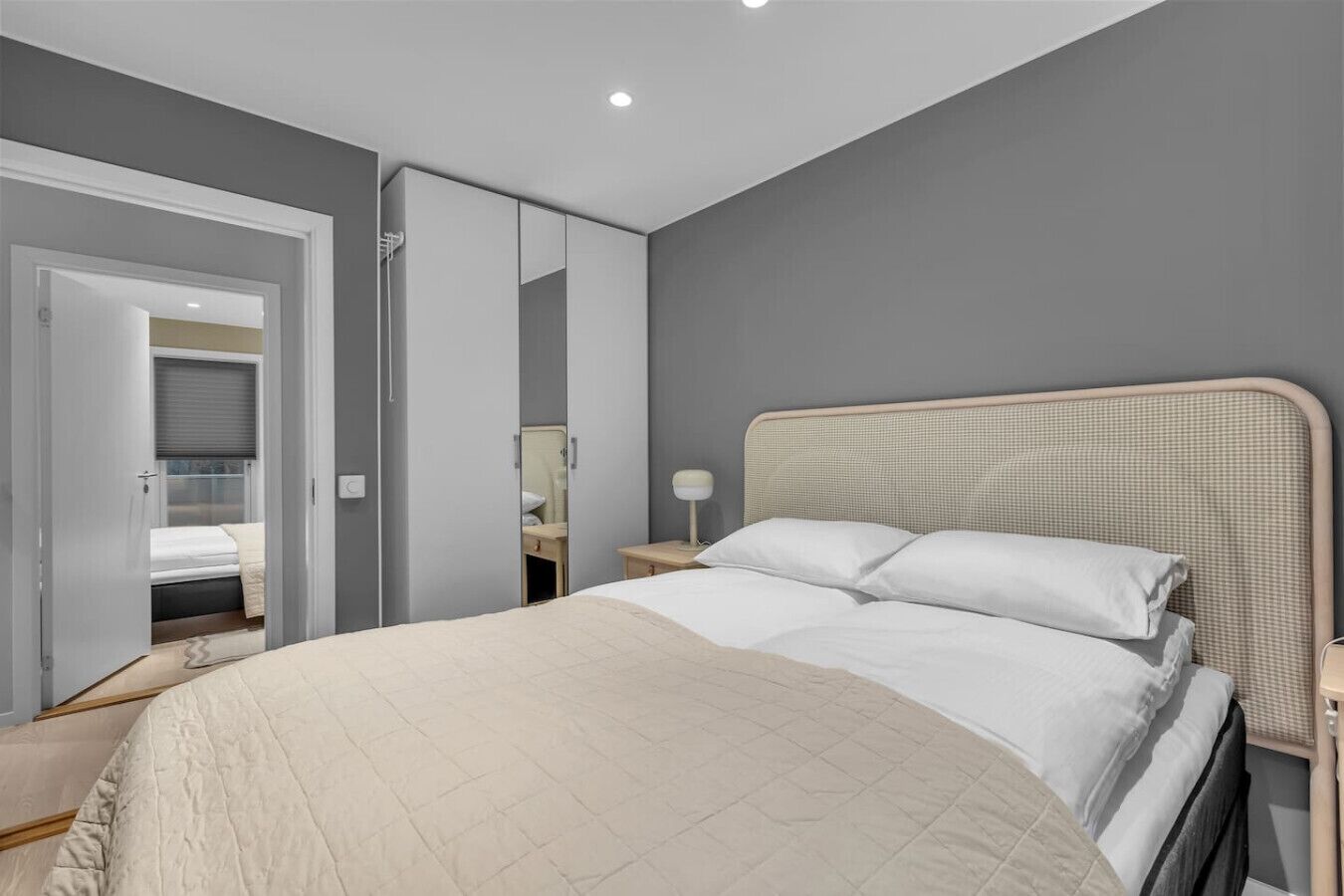 A bedroom with a bed, bedside table, lamp, and a mirror.