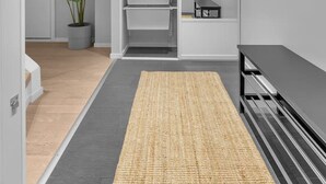 A modern, minimalist hallway with a grey floor, a woven rug, a potted plant, and a built-in shelving unit.
