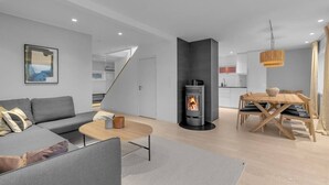 A modern living room with a sofa, coffee table, and a fireplace. There is a dining area with a wooden table and chairs.
