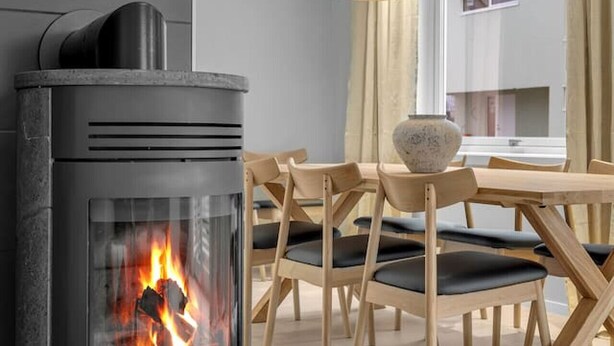 A modern kitchen with a wood-burning stove, wooden chairs, and pendant lights.