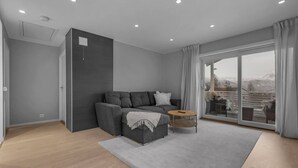 A modern living room with a grey sofa, a small wooden coffee table, and a large sliding glass door leading to a balcony.