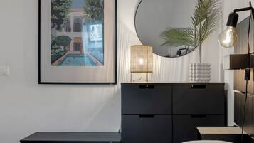 A bedroom with a bed, a dresser, a framed picture, a round mirror, and a lamp.