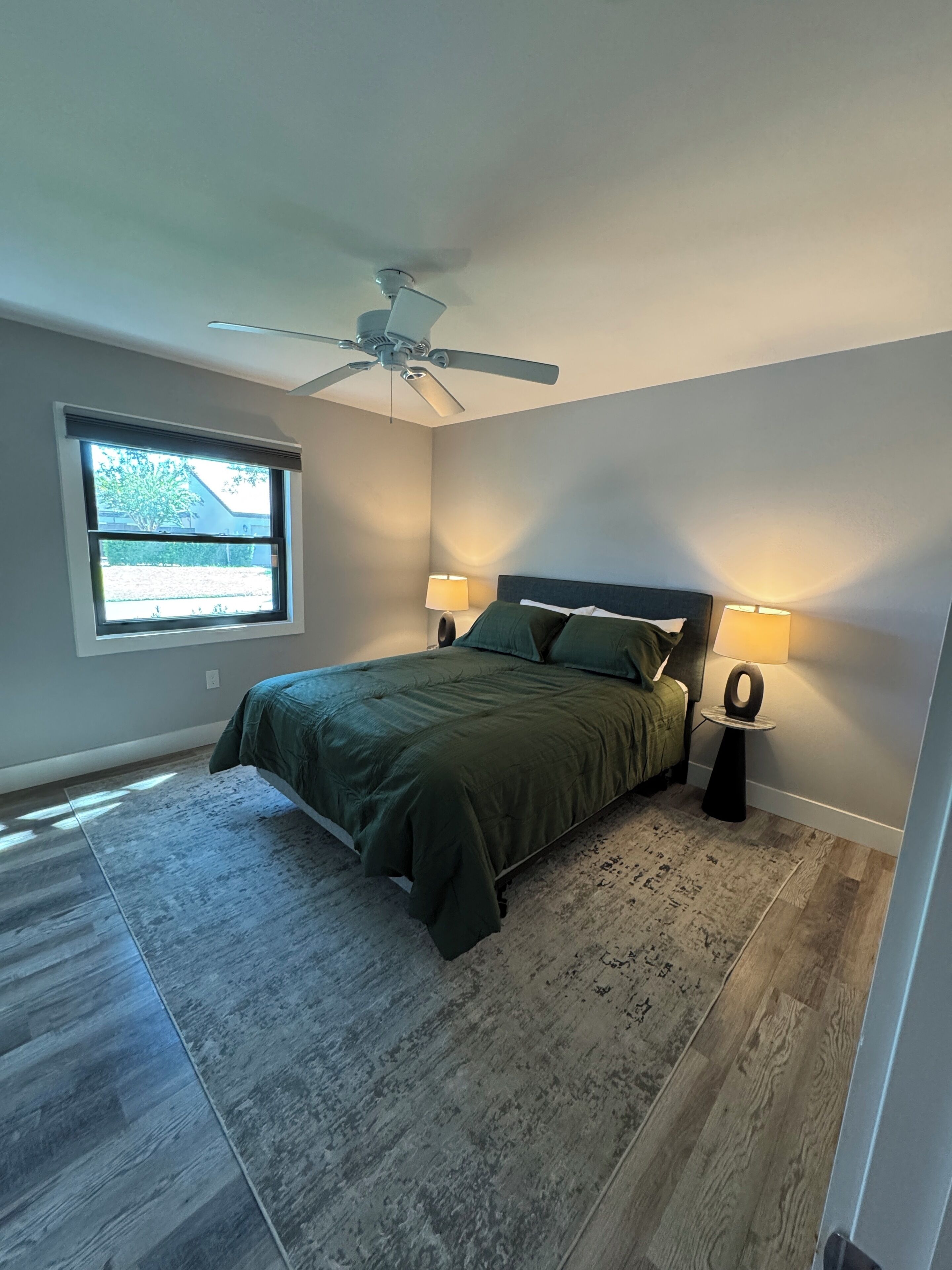 Ein Schlafzimmer mit einem Bett, zwei Nachttischlampen, einem Deckenventilator, einem Fenster und Blick ins Freie.