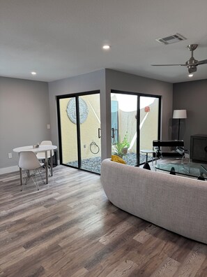 A modern living room with a glass coffee table, a sofa, and a dining area with chairs.