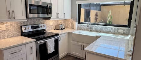 A modern kitchen with white cabinets, stainless steel appliances, a large window, and a view of a cactus garden.