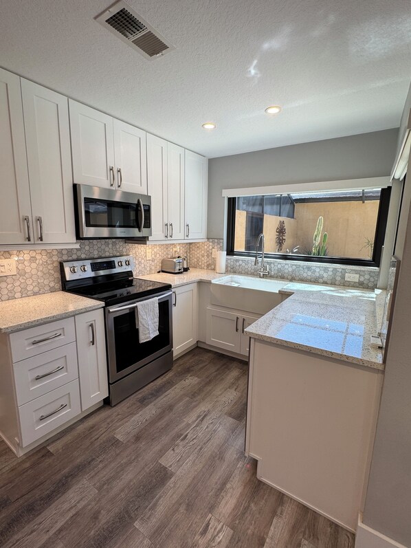 A modern kitchen with white cabinets, stainless steel appliances, a large window, and a view of a cactus garden.
