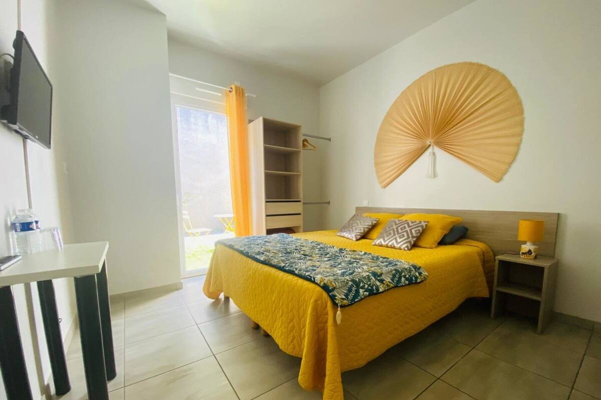 A bedroom with a bed, a TV, a desk, and a large window with curtains.