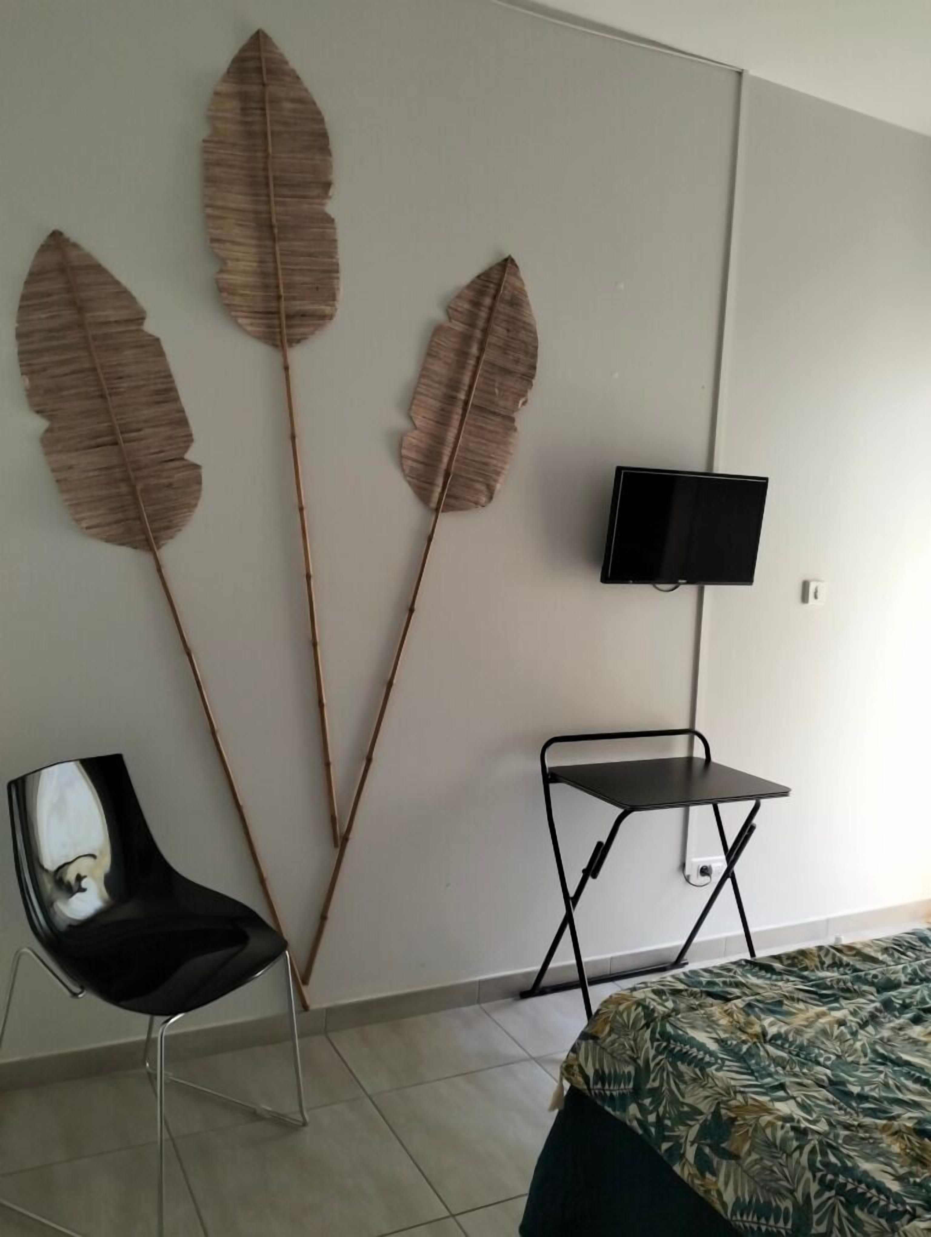 Ein Schlafzimmer mit einem Bett, einem Sessel, einem kleinen Tisch und drei großen Wanddekorationen im Blattstil.