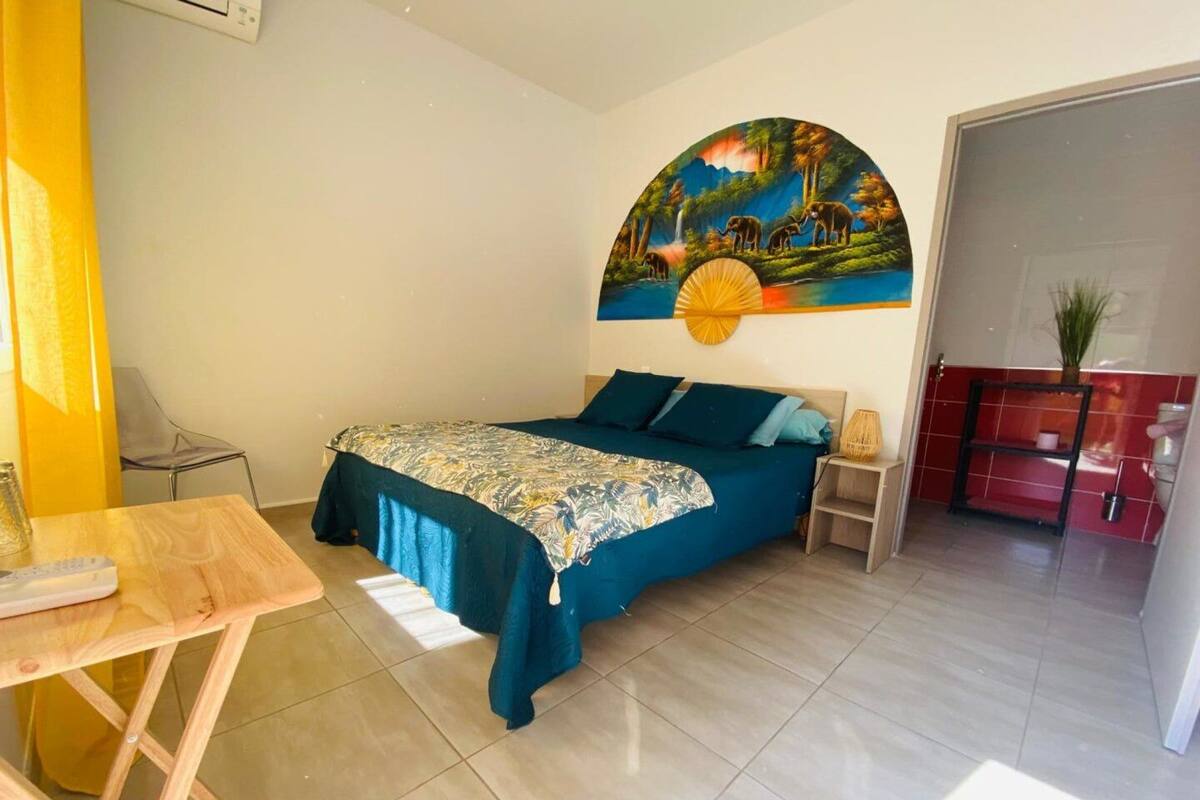 A bedroom with a bed, a desk, a chair, a painting, and a red cabinet.