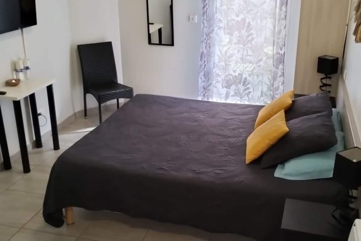 A bedroom with a bed, a chair, a desk, a TV, and a window with curtains.