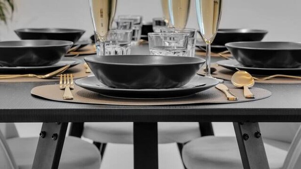 Een eettafel gedekt met zwarte kommen, glazen en een gouden lepel.