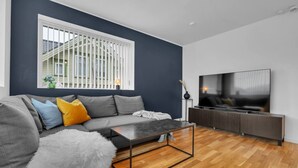 Een moderne woonkamer met een grijze bank, een bijzettafeltje en een televisie op een houten kast.