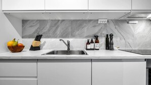 Een moderne keuken met een marmeren spatwand, een RVS-gootsteen en strakke keukenkastjes.