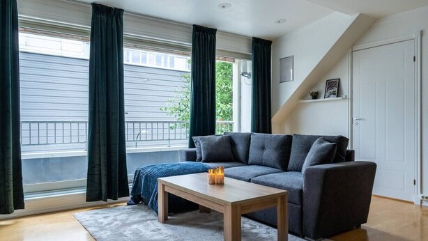 Een moderne woonkamer met een grijze bank, een houten salontafel en een grijs vloerkleed.