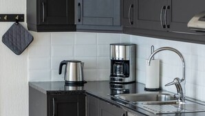 Een moderne keuken met donkere kastjes, een waterkoker, een koffiezetapparaat en een RVS spoelbak.