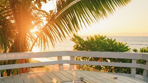 A wooden deck with a glass-top fire pit surrounded by pebbles. - North Shore Luxury Beachfront w/ Hot Tub, Firepit and A/C (Waialua)