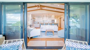A spacious living area with a sofa, coffee table, and a view of the kitchen. - North Shore Luxury Beachfront w/ Hot Tub, Firepit and A/C (Waialua)