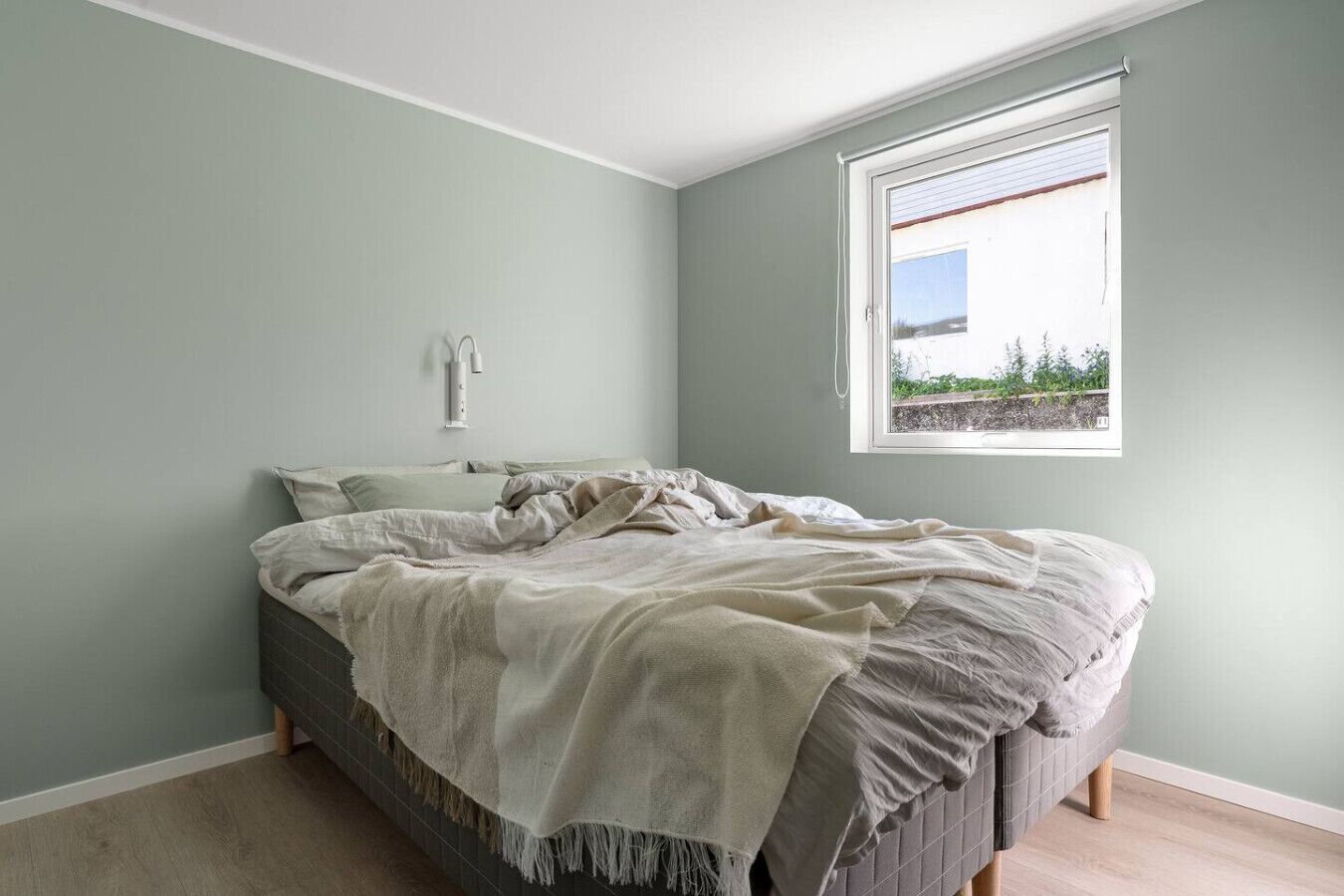 A bedroom with a bed, a window, and a wall-mounted light fixture.