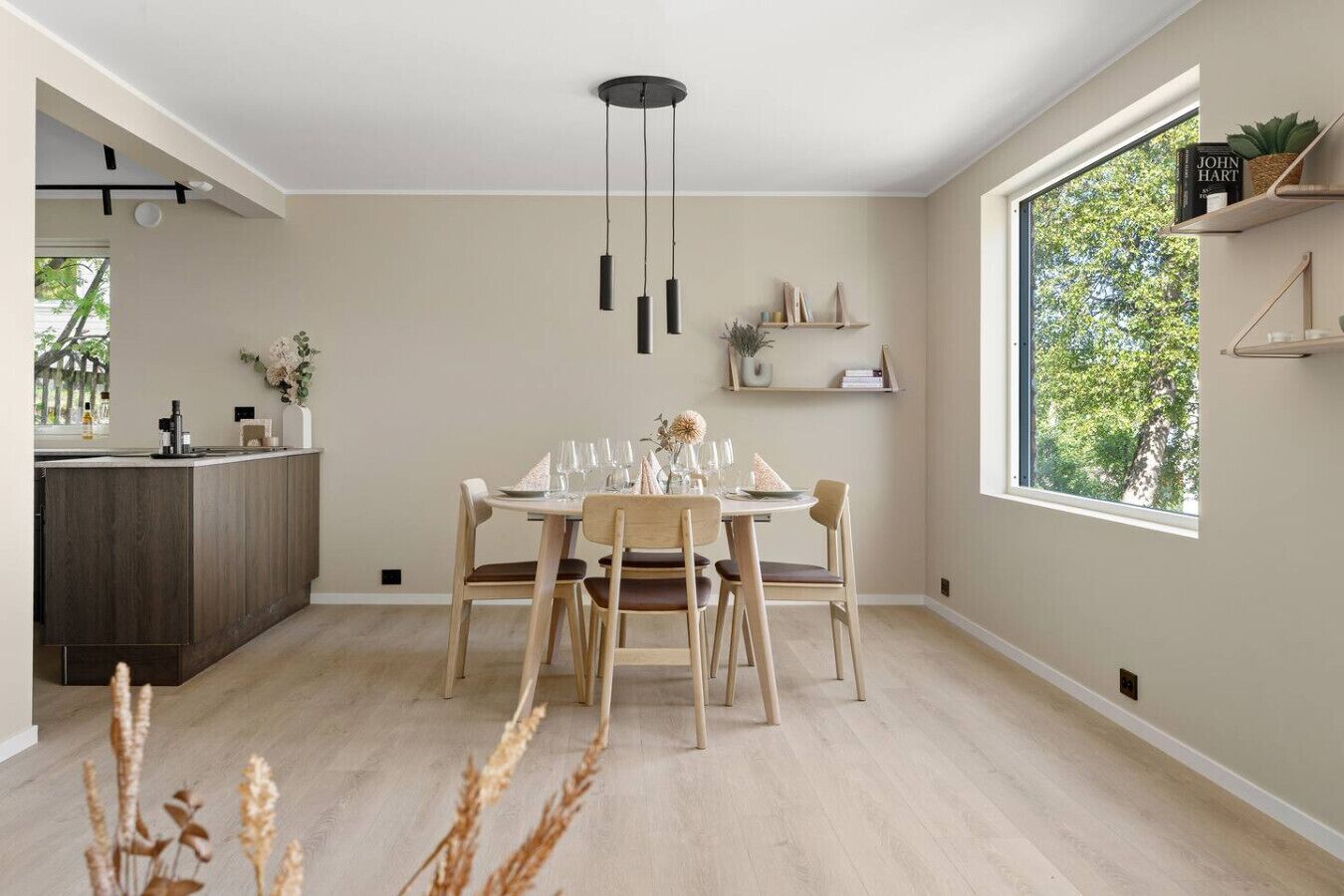 Un comedor moderno con mesa y sillas de madera, una cocina con armarios de madera oscura, y un ventanal con vistas a árboles.