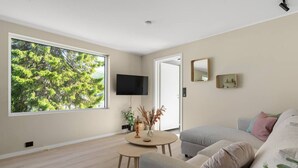 Ein modernes Wohnzimmer mit großem Fenster, Flachbildfernseher, rundem Couchtisch und grauem Sofa.