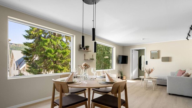 Ein moderner Essbereich mit einem runden Tisch, zwei Stühlen und Blick auf einen Baum durch große Fenster.