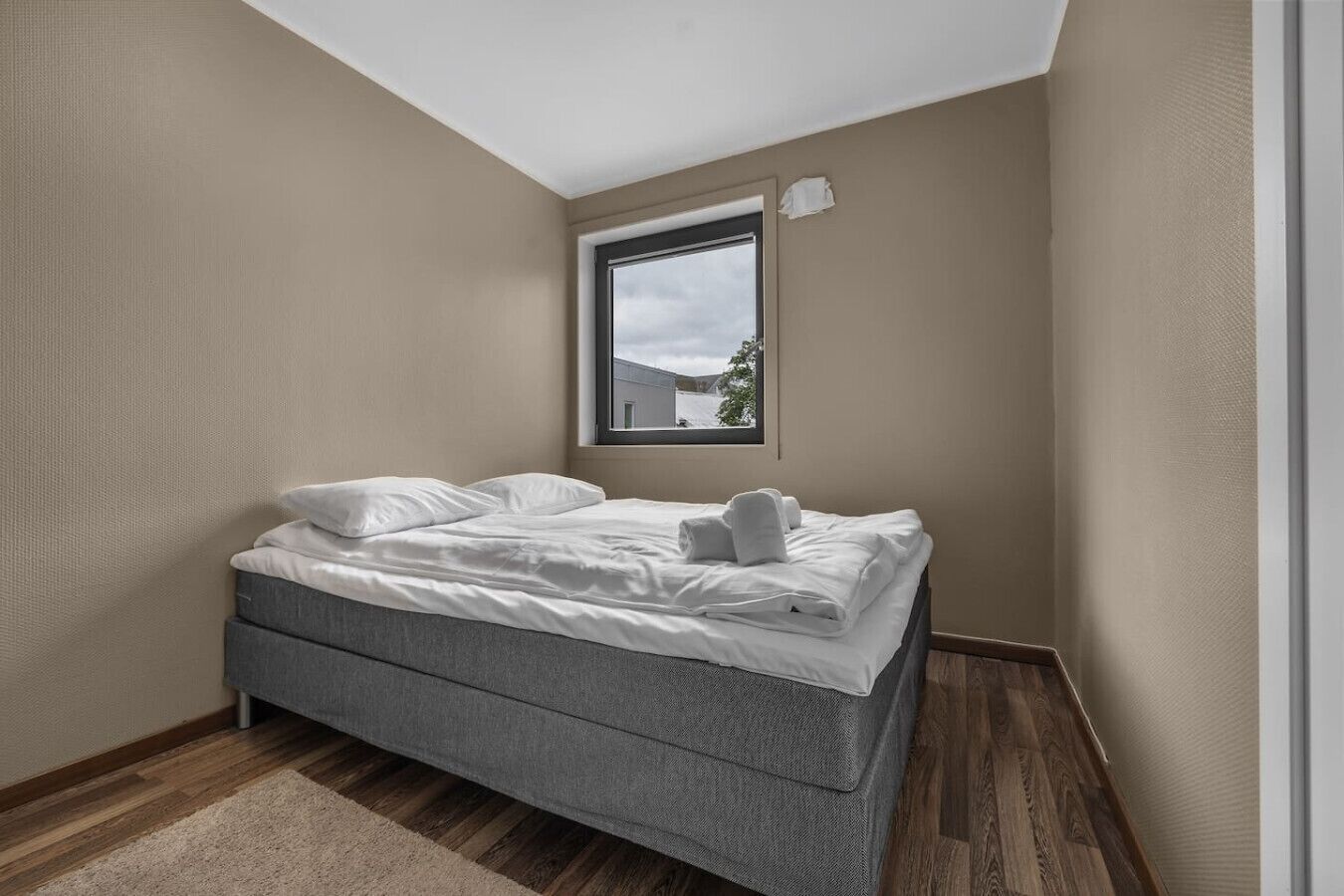 Quarto com cama, janela e vista para um edifício.