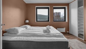 Een slaapkamer met een bed, twee ramen, een radiator en een kledingkast.