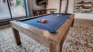 Ein Billardtisch mit Kugeln, ein an der Wand befestigter Fernseher und eine Sitzecke mit Tischen und Stühlen.