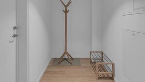 Un couloir étroit doté d’un plancher en bois, d’un porte-manteau, d’un petit banc en bois et d’une porte située sur le côté gauche.
