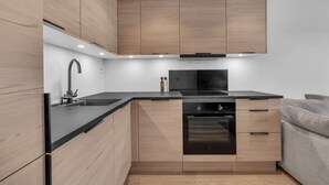 Une cuisine moderne avec des meubles en bois, un plan de travail noir, un four encastré et un évier.