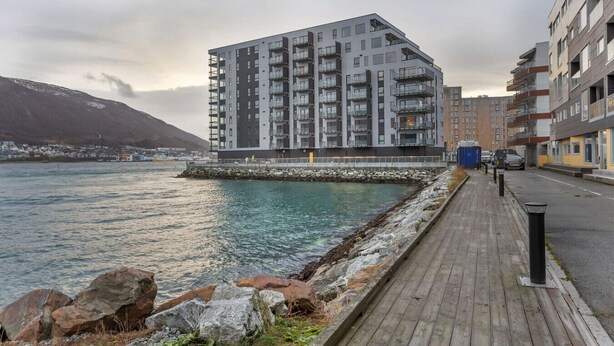 Un immeuble moderne à plusieurs étages, doté de balcons, situé au bord de l’eau, avec une promenade en bois.