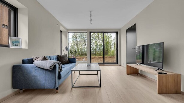 Un salon moderne avec un canapé, une table basse, un téléviseur et de grandes fenêtres.