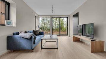 A modern living room with a sofa, coffee table, TV, and large windows.