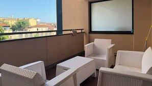 A balcony with white wicker furniture, a projector screen, and a view of buildings in the distance.