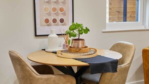 A round wooden table with a dark cloth, surrounded by four beige upholstered chairs. A small potted plant and a decorative tray are on the table.