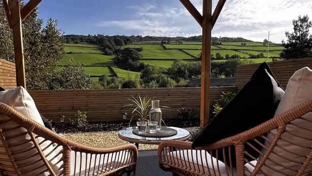 A covered outdoor seating area with wicker chairs and a round table, overlooking a green landscape.