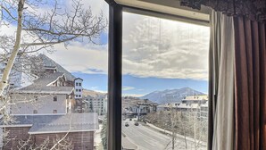 A room with a large window offering a view of a cityscape, including buildings and mountains. - Grand Lodge Crested Butte | King Suite, Walk to Lifts, Pool & Hot Tub, View (Crested Butte)