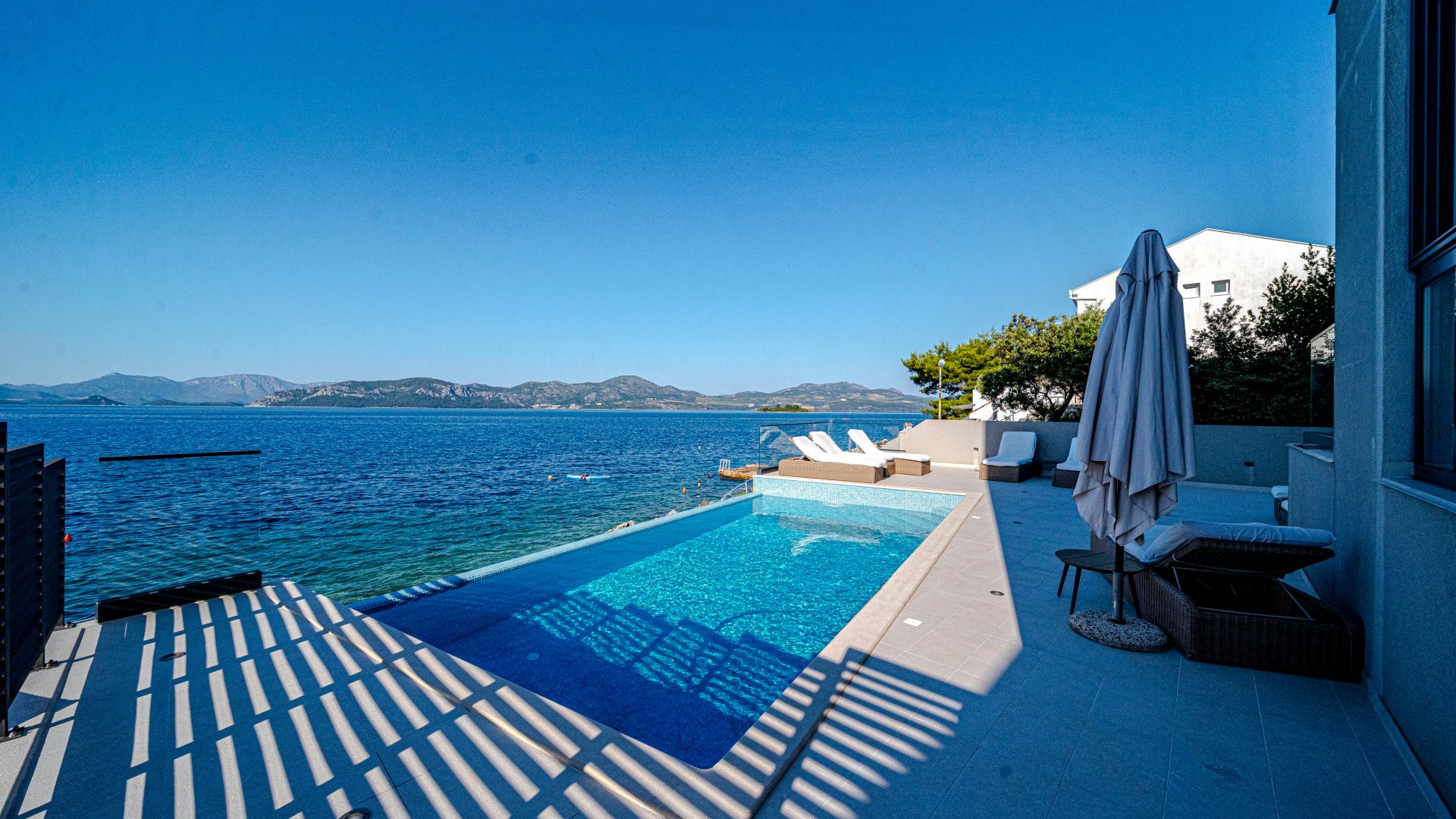 Ein Pool mit Blick auf Meer und Berge, Sitzgelegenheiten im Freien und ein überdachter Bereich.