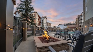Un área de estar al aire libre con una chimenea, rodeada de sillones reclinables y una piscina al fondo.