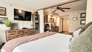Un dormitorio con una cama grande, un aparador, un televisor y una kitchenette al fondo.