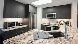 Una cocina moderna con armarios oscuros, electrodomésticos de acero inoxidable y encimera de granito.