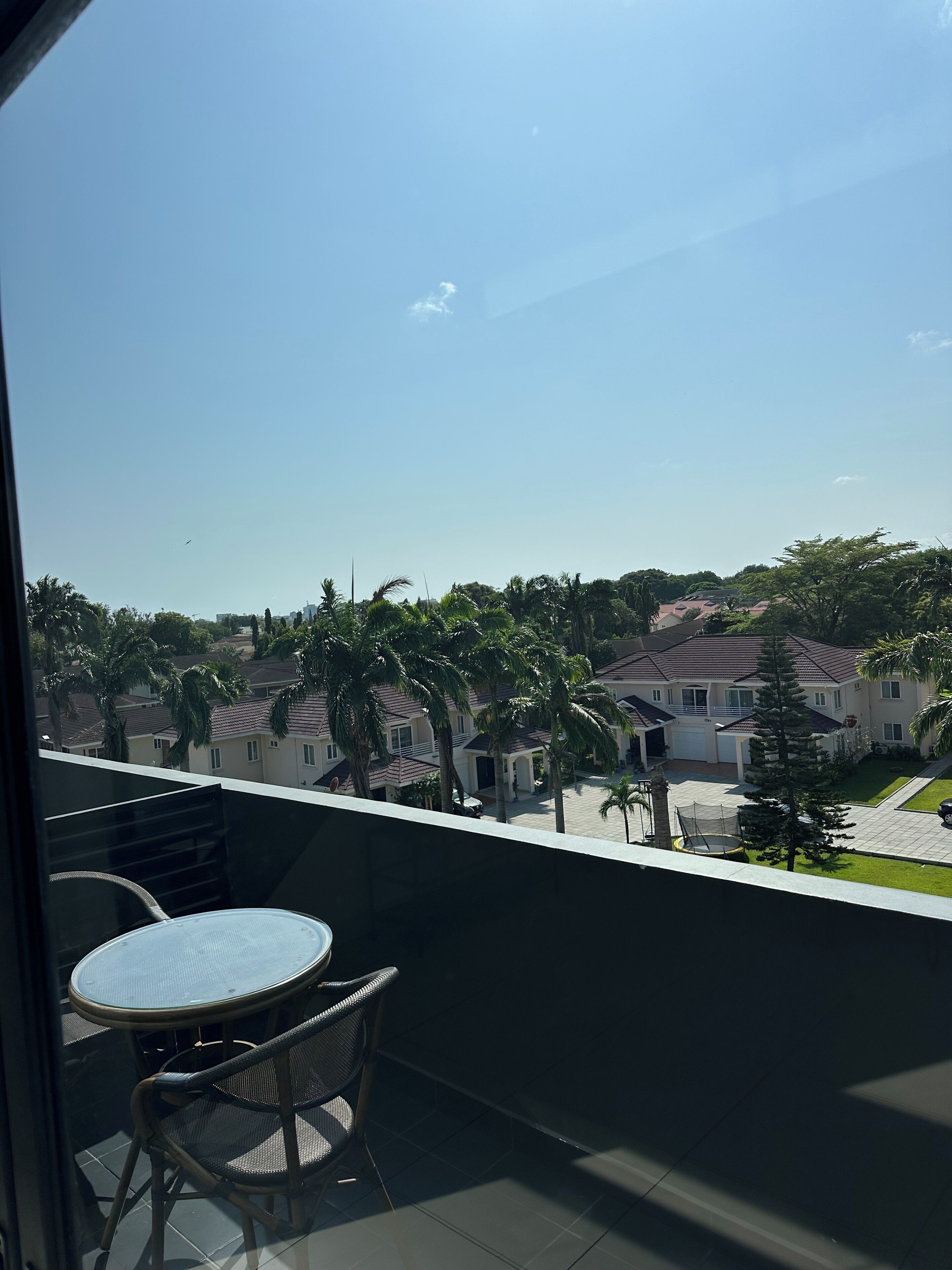 A balcony with a table and chairs, overlooking a residential area with houses and palm trees.