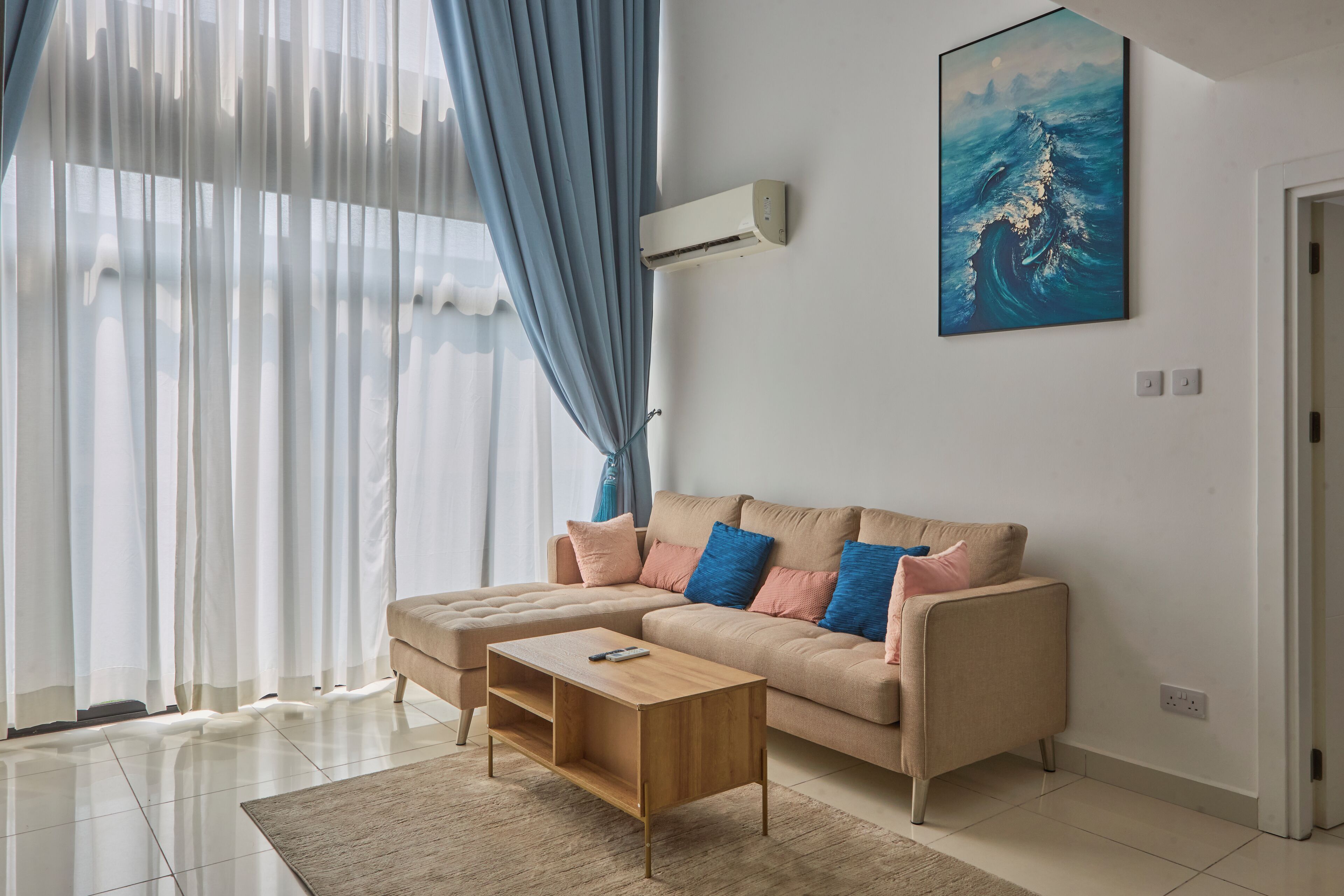 A modern living room with a beige sofa, a wooden coffee table, and a large window with sheer curtains.