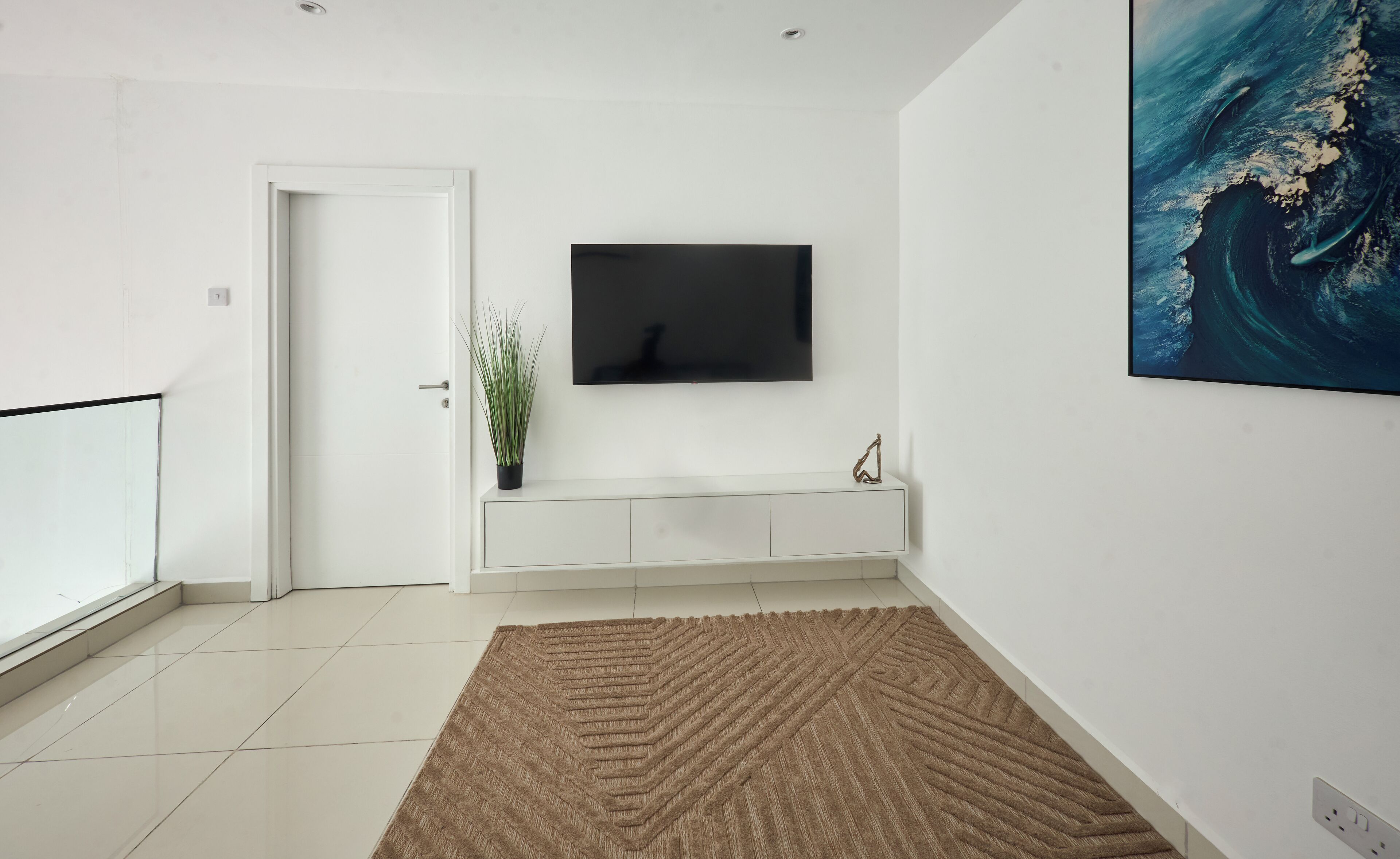 Een moderne woonkamer met een flatscreen televisie aan de muur, een potplant en een decoratieve sculptuur op een witte consoles.
